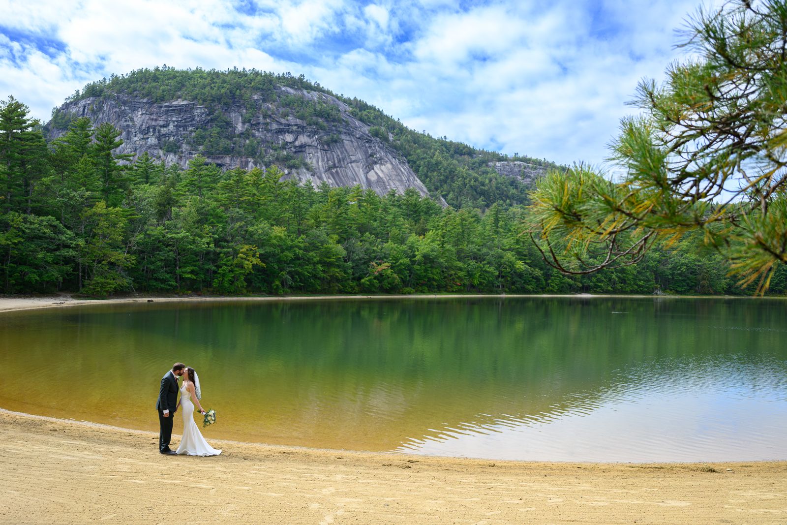 Couple on the Echo Lake State Park beach with Cathedral Ledge rising above the water in North Conway