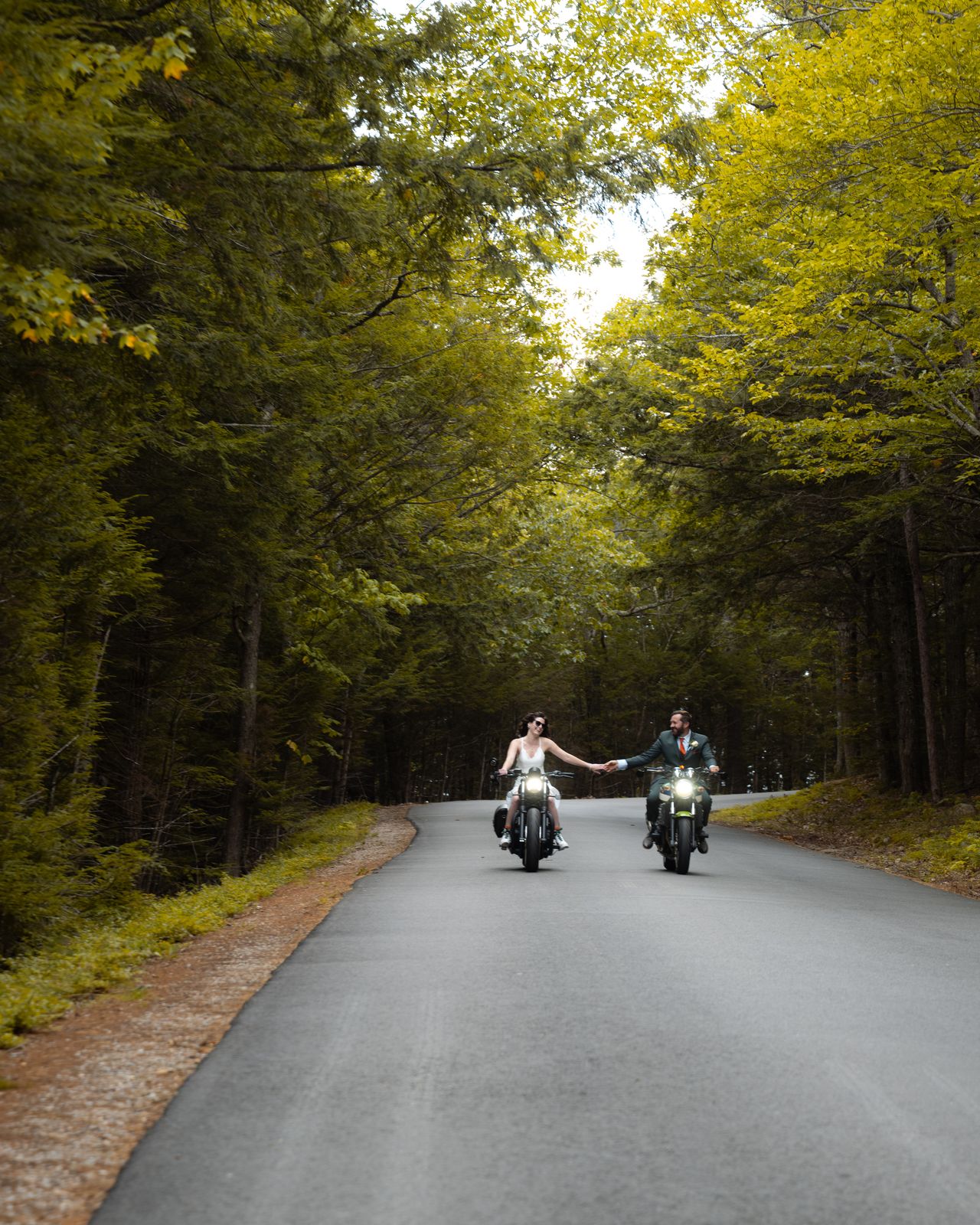 Bride and groom riding motorcycles side by side up the tree lined Cathedral Ledge road